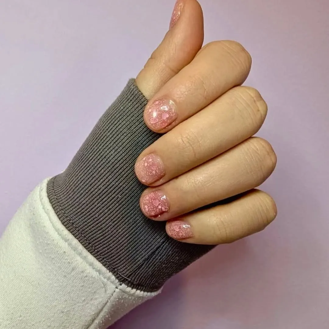 Mano con manicure in gel rosa cipria e glitter argento, su sfondo lilla